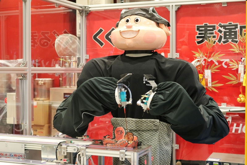 A dual-arm robot applies sauce and mayonnaise to takoyaki at HCI's booth 